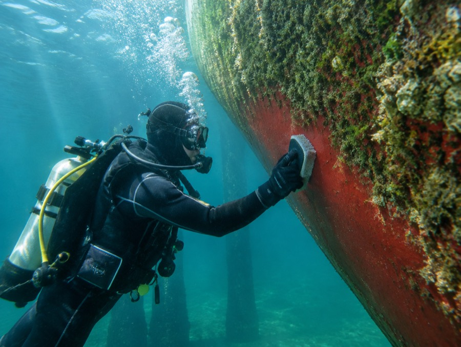 A diver underwater scrubbing growth off a boat hull